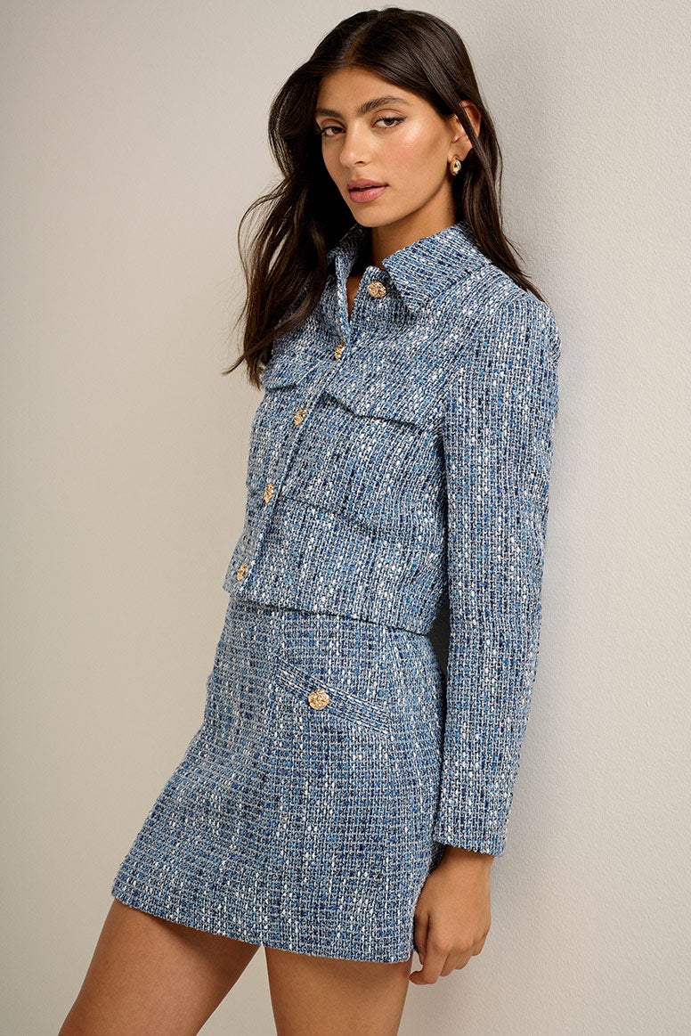 model wearing blue boucle jacket and matching mini skirt with dark hair looking into the camera