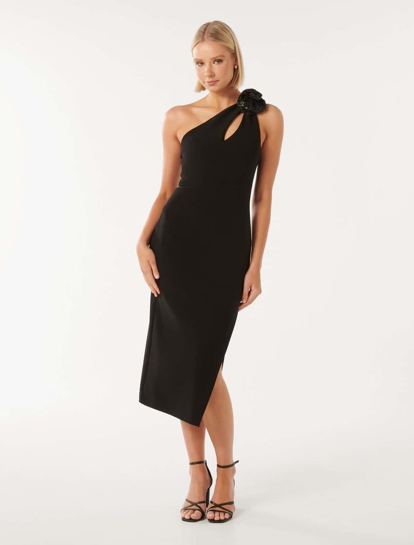 model with blonde bob wearing a black bodycon dress with a corsage detail at the shoulder and strappy black heels